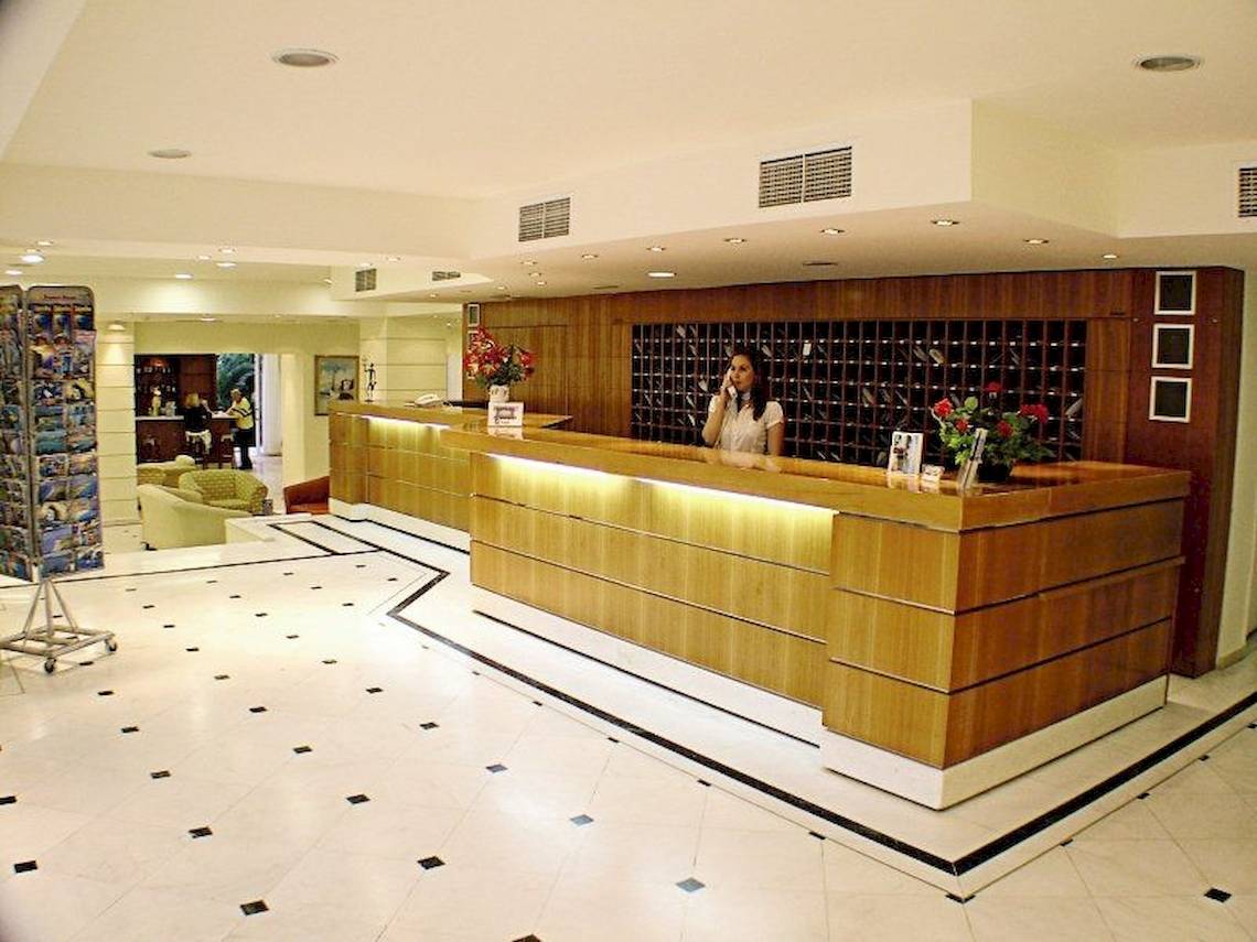 Empfangsbereich des Poseidon Beach Hotels mit Rezeptionistin am Schalter.