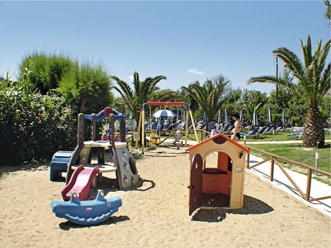 Kinderspielplatz im Poseidon Beach Hotel mit Sand, Spielgeräten und Sonnenschirmen.