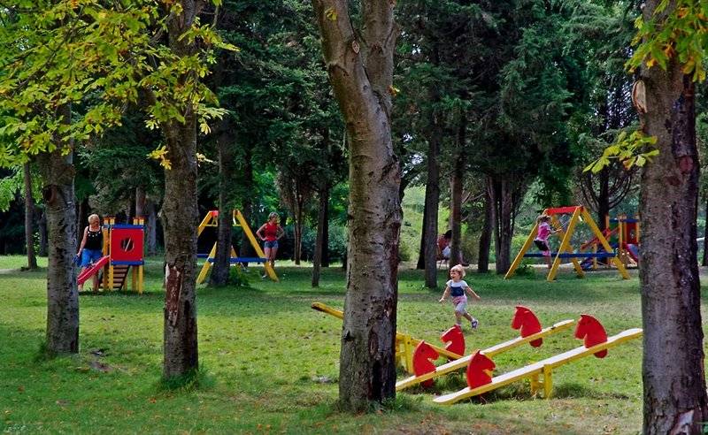 Kinderspielplatz im Freien im Sol Nessebar Palace Hotel mit Bäumen und Spielgeräten.