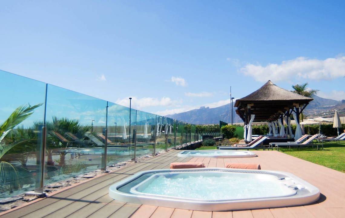 Außenbereich des Gran Melia Palacio de Isora Hotels mit zwei Whirlpools, einem Pool und Sonnenliegen.