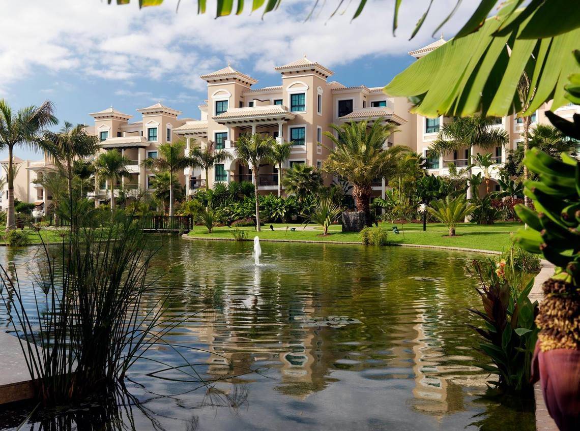 Gran Melia Palacio de Isora Hotel mit Teich und Palmen im Vordergrund.