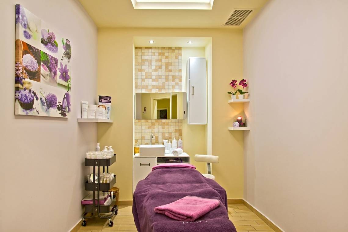 Behandlungsraum im Spa des La Marquise Luxury Resort Complex mit hellen Wänden, Möbeln und einer Liege mit violettem Handtuch.