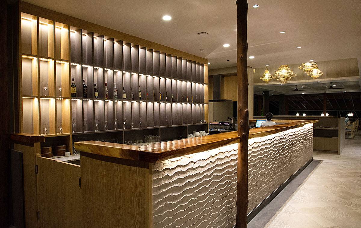 Innenansicht der Bar im Andaman Cannacia Resort mit Holztheke und beleuchteten Regalen.
