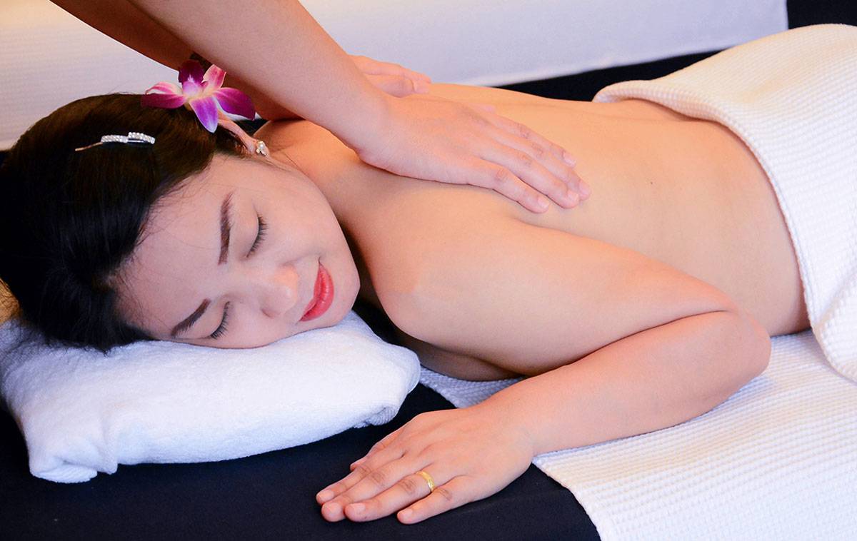 Frau im Andaman Cannacia Resort genießt eine Massage mit einem weißen Handtuch und einer Blume im Haar.