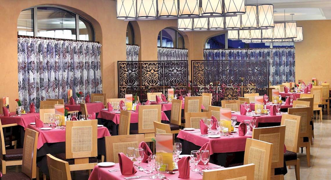 Restaurant im Barcelo Maya Palace Hotel mit vielen gedeckten Tischen und dekorativen Elementen.