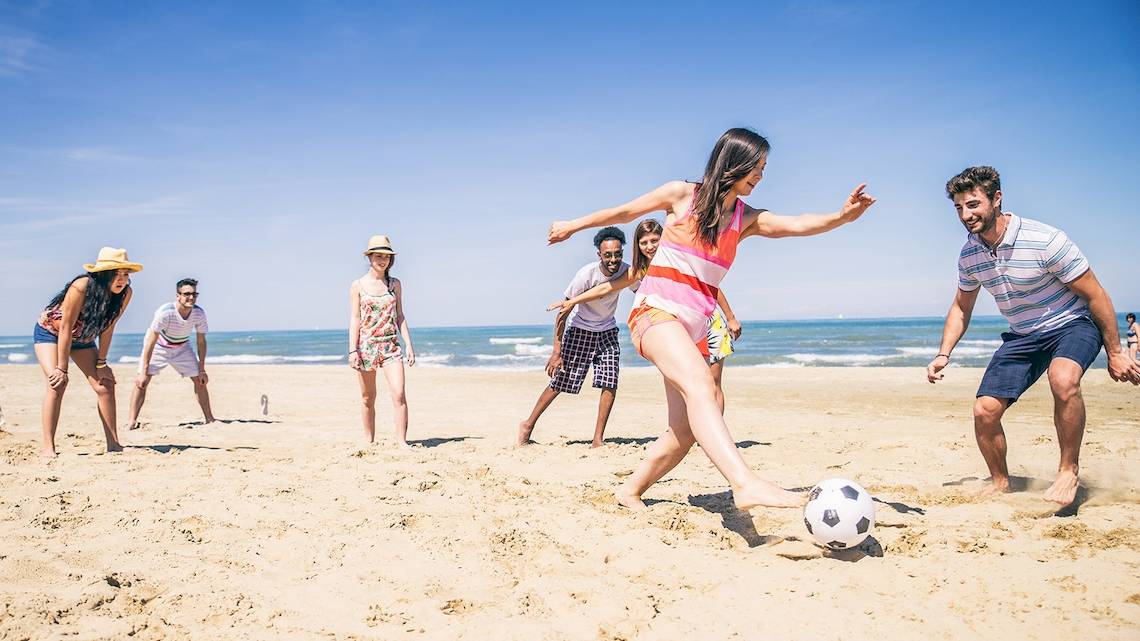 Gruppe von Menschen, die Fußball auf dem Strand spielen, bei klarem Himmel.