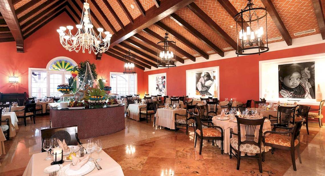 Innenbereich des Restaurants im Barcelo Maya Palace Hotel mit roten Wänden, Tischdecken und Kronleuchtern.
