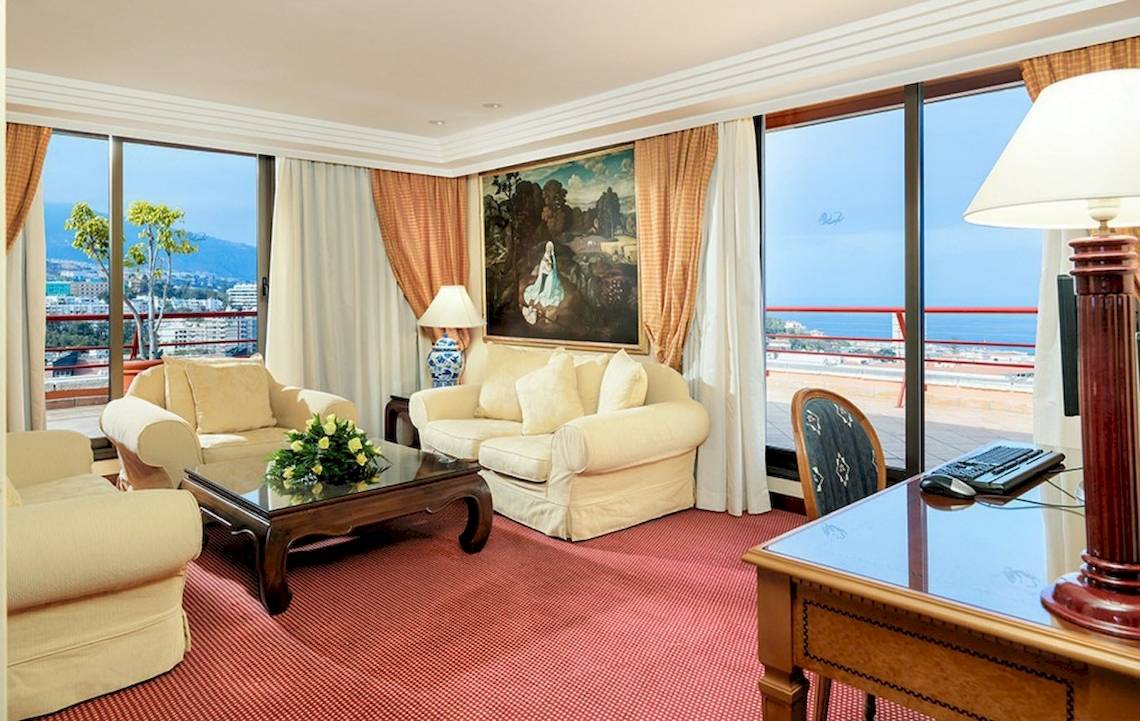 Wohnzimmer mit Meerblick im Botanico Hotel mit Sofas, Tisch, Lampe und Gemälde.