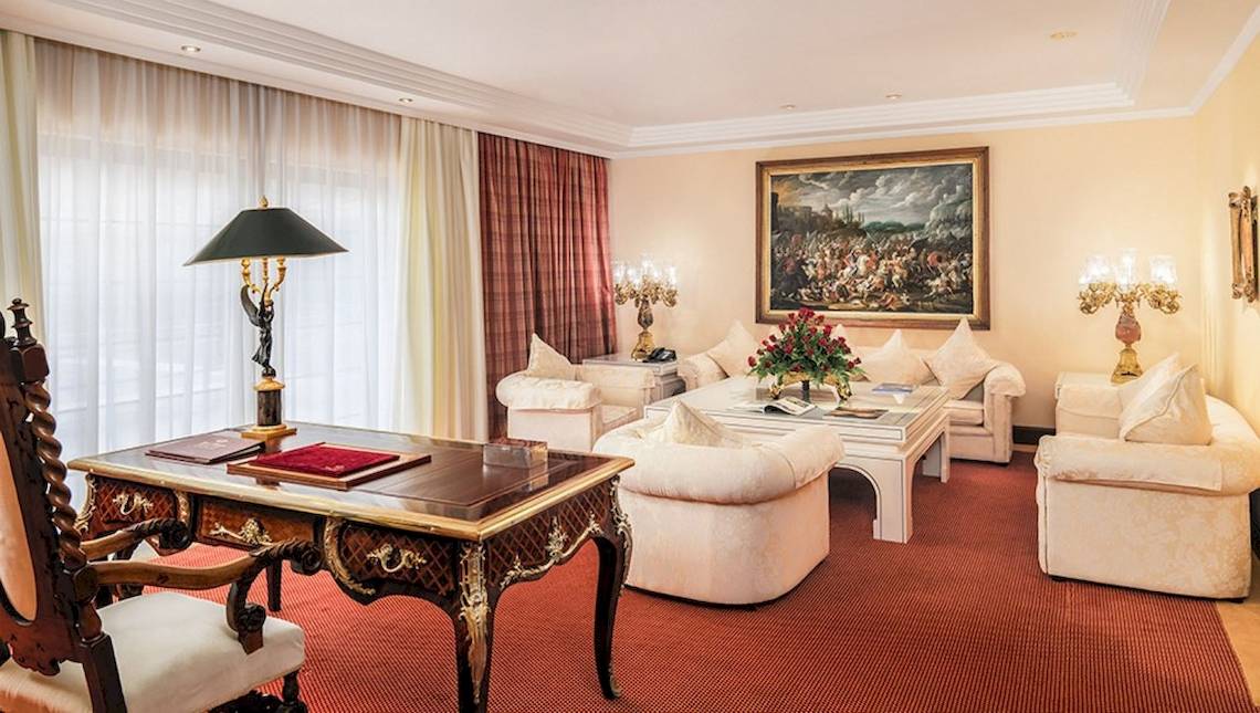 Luxuriöses Hotelzimmer mit einem Arbeitstisch, Sofas, Lampen und einem großen Gemälde an der Wand.