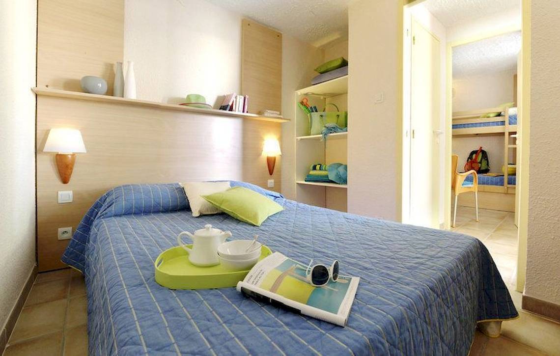 Ein geräumiges Zimmer im Belambra Clubs Pineto mit einem Bett, Büchern, einem Tisch und einer Lampe.