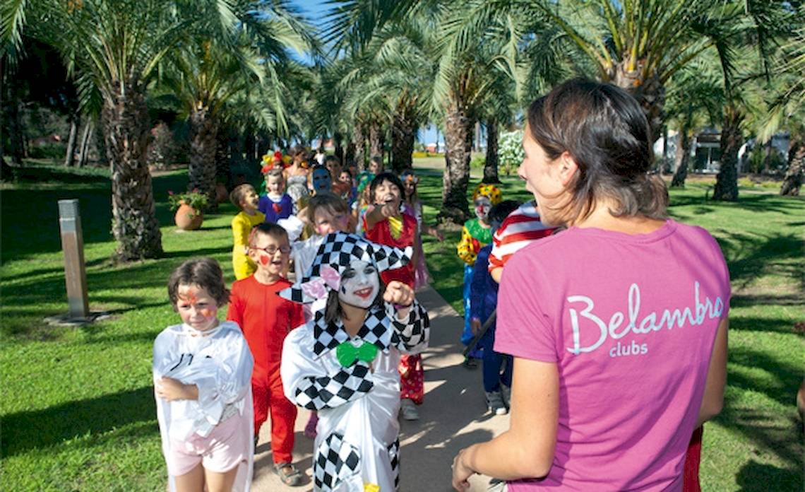 Kinder in Kostümen bei Belambra Clubs Pineto, begleitet von einer Frau in Pink, vor Palmen