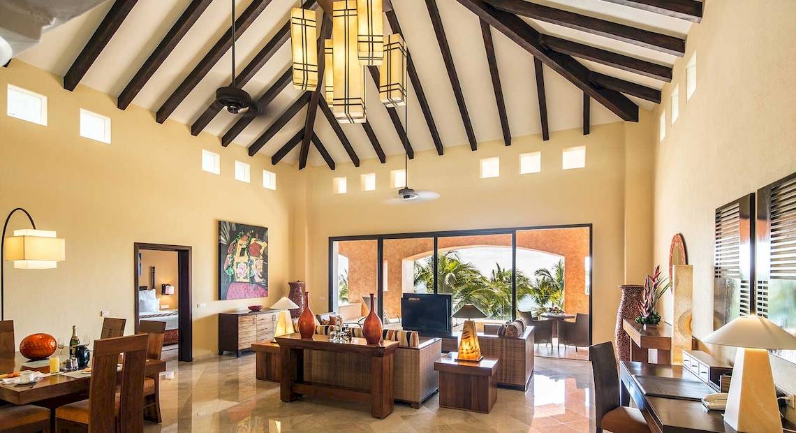 Das Wohnzimmer des Barcelo Maya Palace mit hohen Decken, Holzmöbeln und einem Panoramafenster.