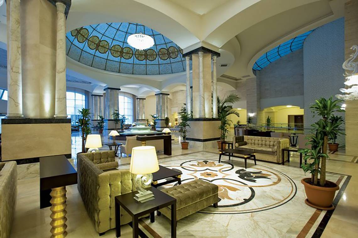 Lobby des Melas Lara Hotels mit gemustertem Boden, Sofas, Lampen und Pflanzen.