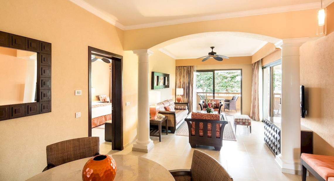 Wohnzimmer im Barcelo Maya Palace mit Möbeln, Teppich, Fernseher, Spiegel und Deckenventilator.