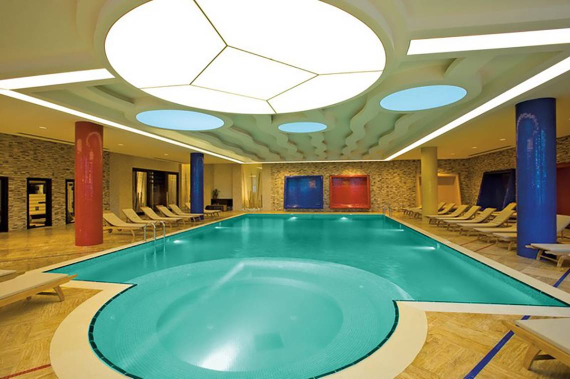 Innenpool des Melas Lara Hotels mit Loungeliegen und bunten Säulen.