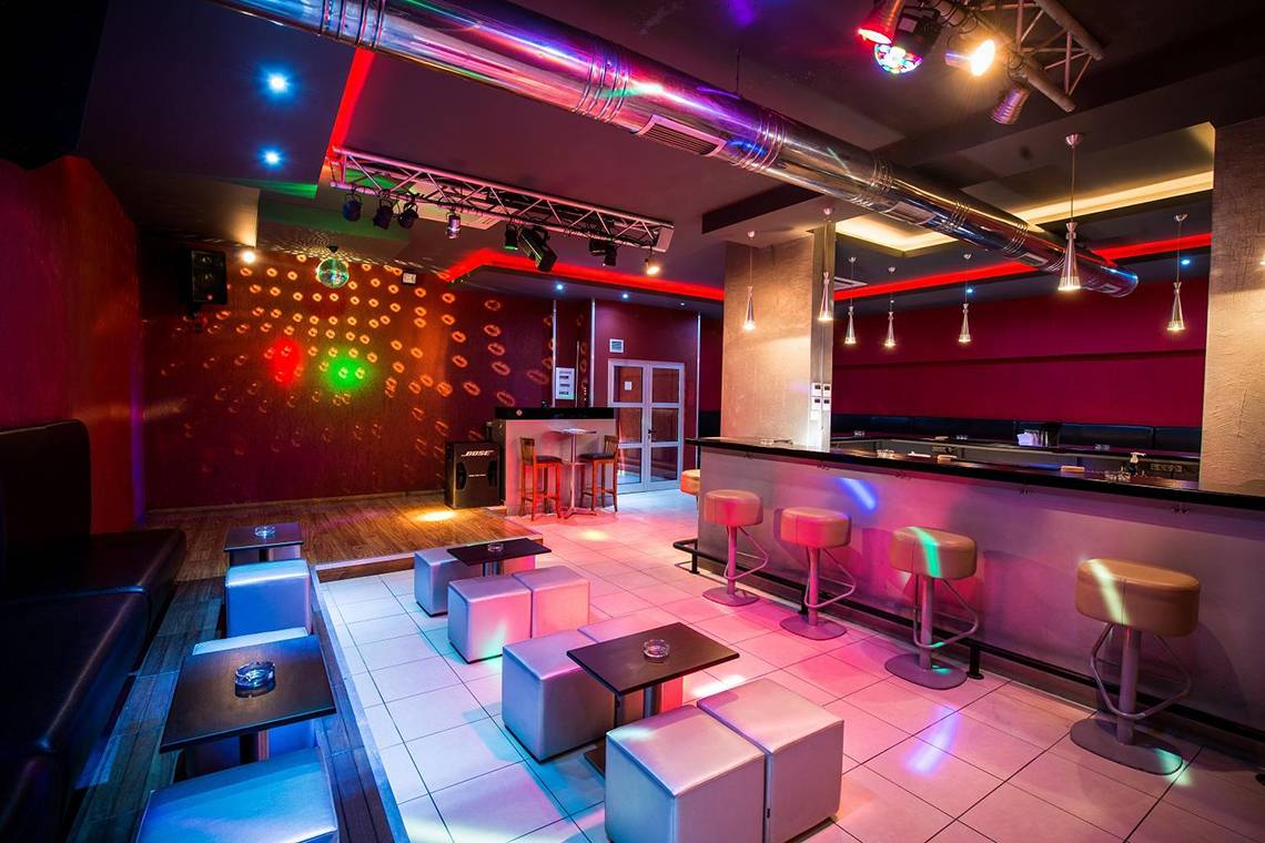 Innenansicht einer Disco mit Bar, Barhockern und Tischchen sowie farbiger Beleuchtung.