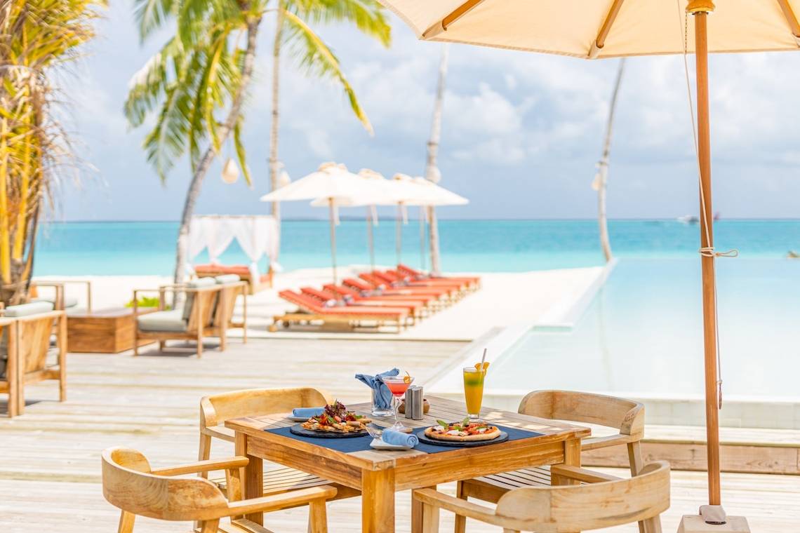 Terrasse des Sun Siyam Iru Veli Hotels mit Esstisch und Getränken vor einem Pool