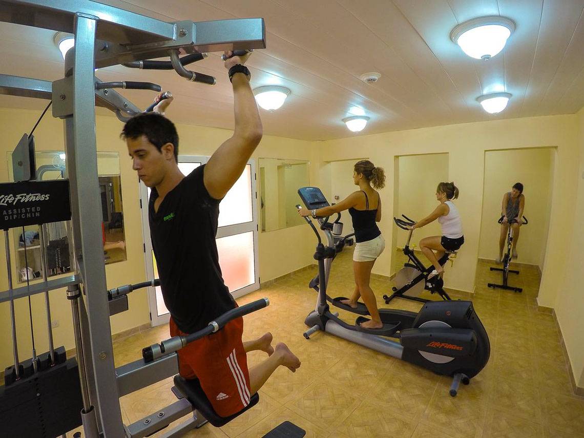 Fitnessstudio im ROC Arenas Doradas Hotel mit drei Personen, die an verschiedenen Geräten trainieren.
