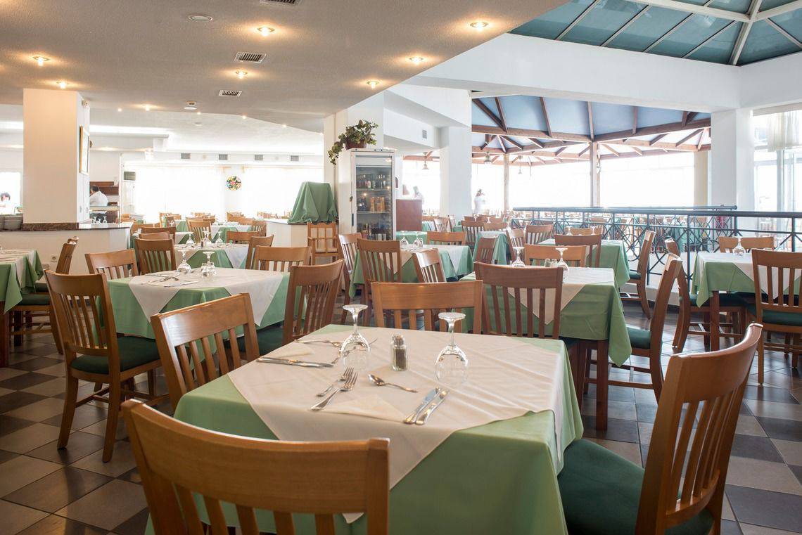 Innenansicht des Restaurants im Mastichari Bay Hotel mit grün-weiß gedeckten Tischen und Stühlen.