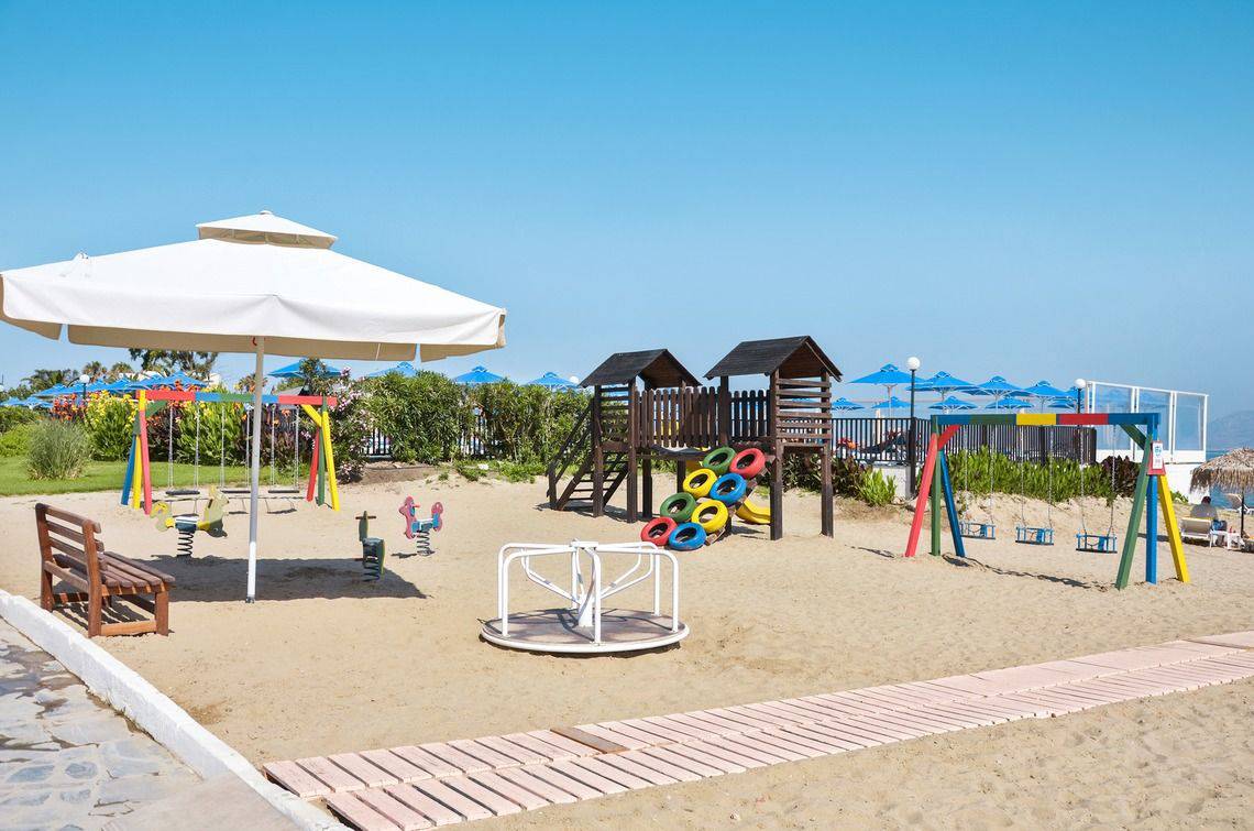 Kinderspielplatz am Strand des Mastichari Bay Hotels mit bunten Schaukeln und Geräten.