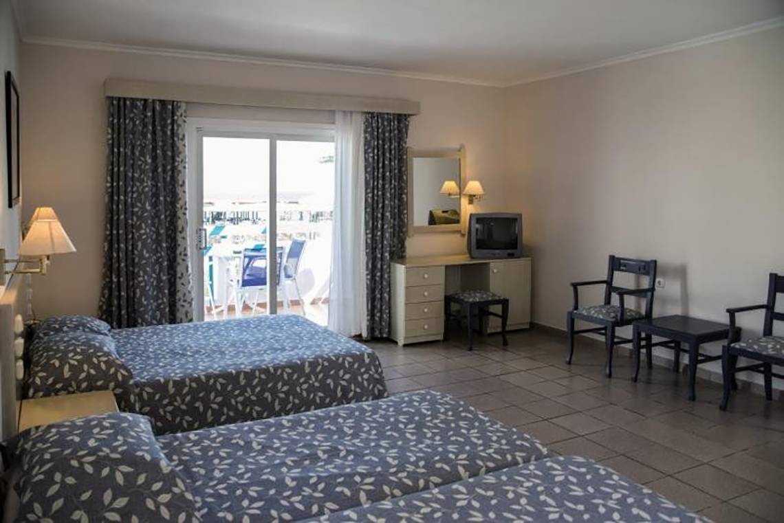 Doppelzimmer im Mastichari Bay Hotel mit zwei Betten, Fernseher, Schreibtisch und Balkonblick.