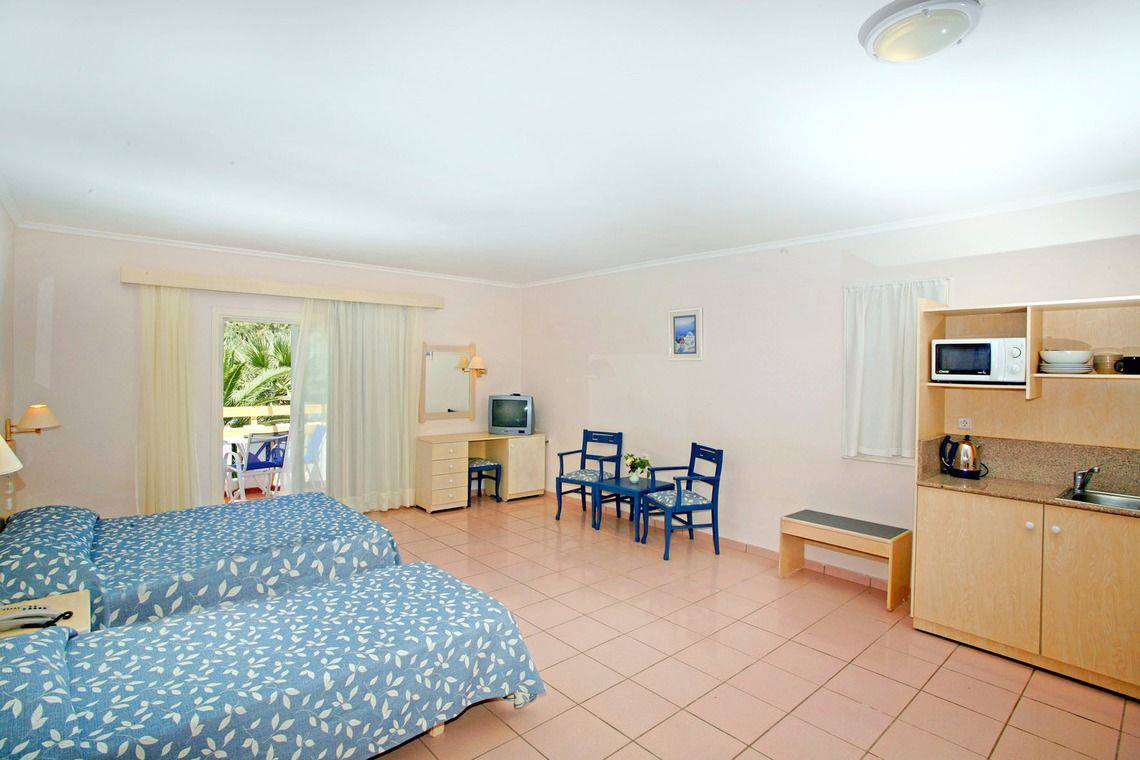 Doppelzimmer im Mastichari Bay Hotel mit zwei Betten, Schreibtisch, Fernseher, Stühlen und Küche.