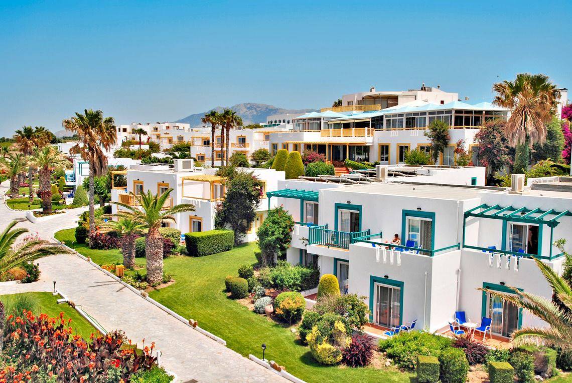 Luftaufnahme des Mastichari Bay Hotels mit weißen Gebäuden, blauen Balkonen und grünen Gärten.