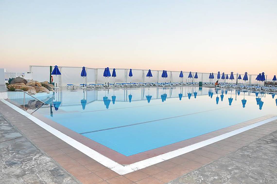 Außenpool des Mastichari Bay Hotels mit blauen Sonnenschirmen und leeren Sonnenliegen.