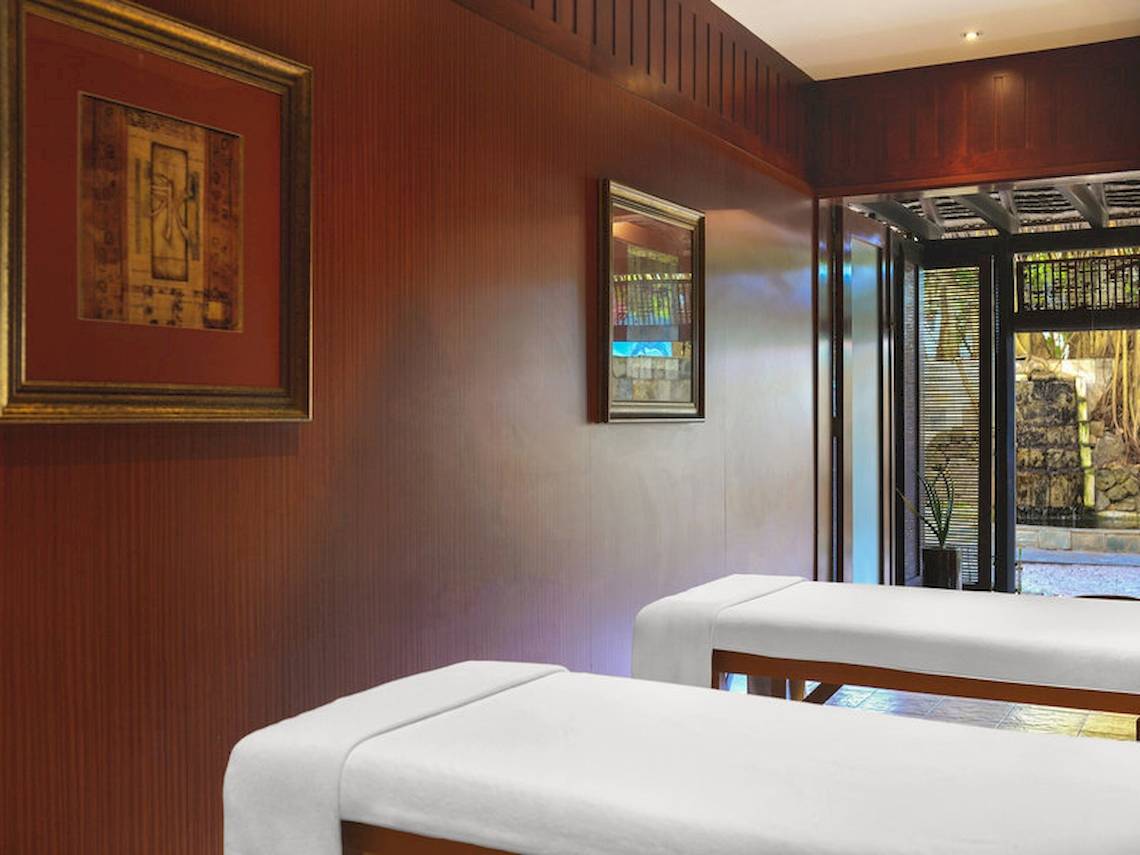 Massageraum im Le Meridien Ile Maurice Hotel mit zwei weißen Massageliegen und dekorativen Rahmen an der Wand.