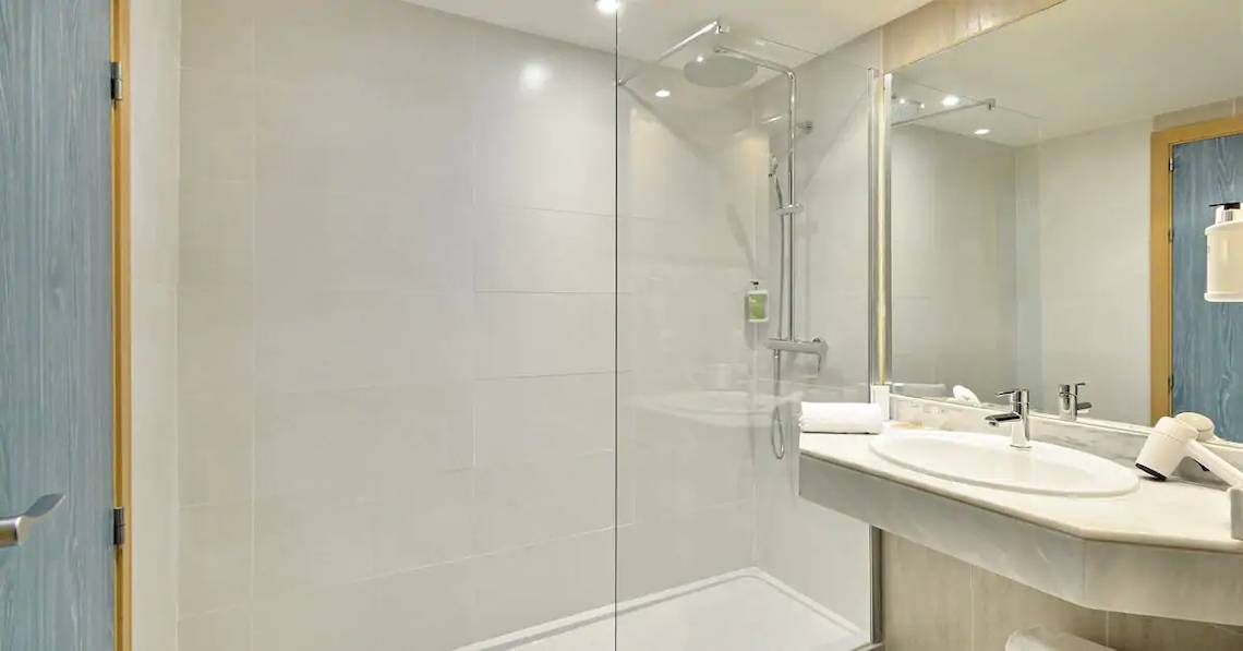 Badezimmer im Sol Barbados Hotel mit Glasdusche, Waschbecken und Spiegel.