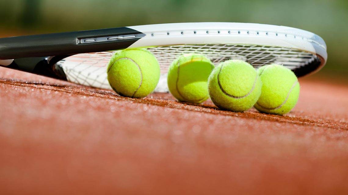 Tennisschläger und Tennisbälle auf einem roten Tennisplatz.