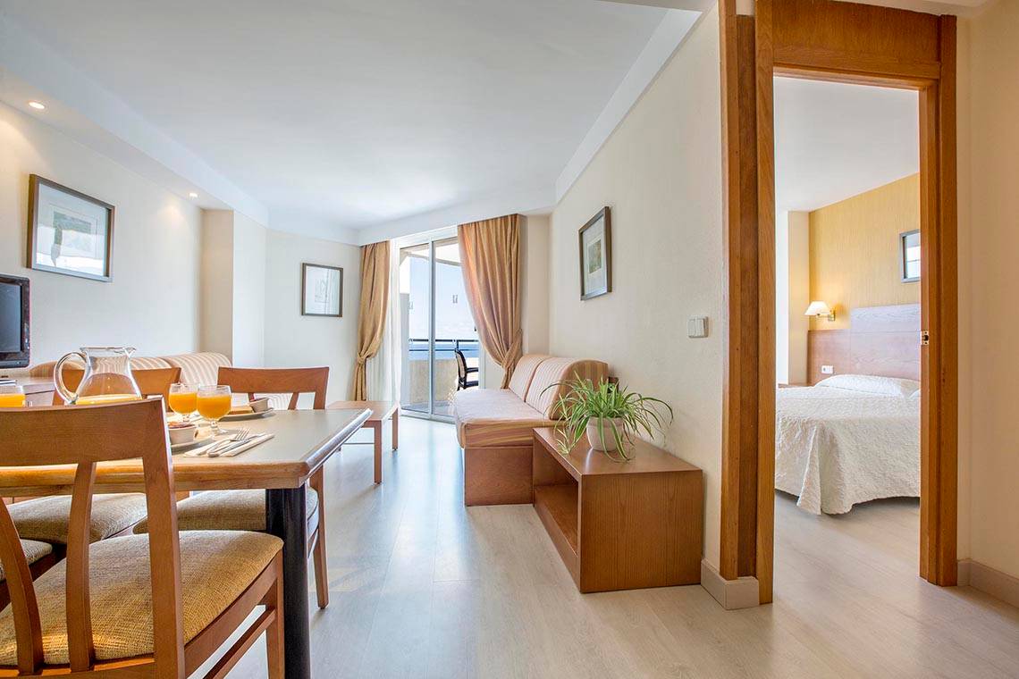 Innenansicht eines Zimmers im Hipotels Bahia Grande Hotel mit Esstisch, Sofa und Bett.