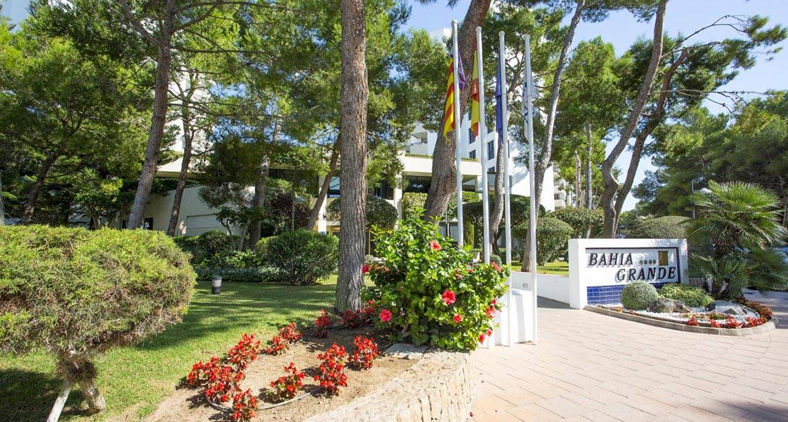 Eingang zum Hipotels Bahia Grande Hotel mit Schild und Flaggen vor einem grünen Rasen.