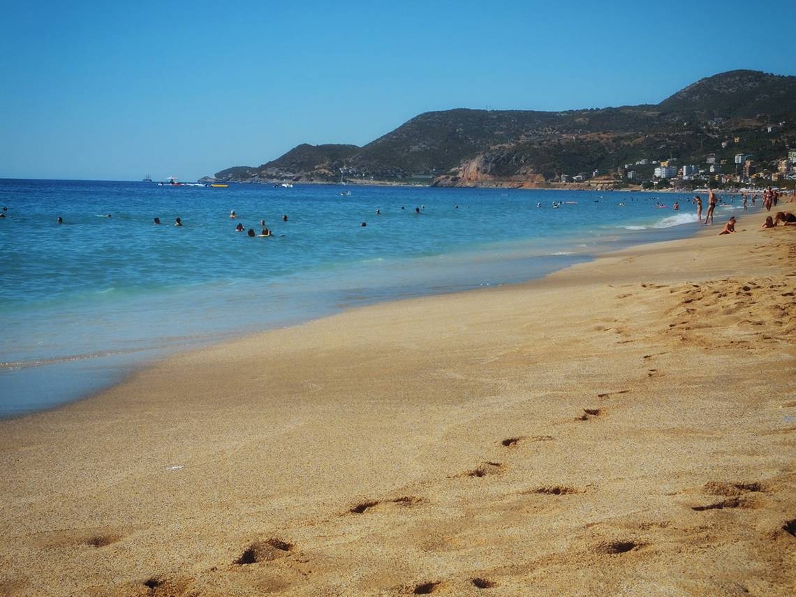 Leute baden an einem Strand, während Berge im Hintergrund zu sehen sind.