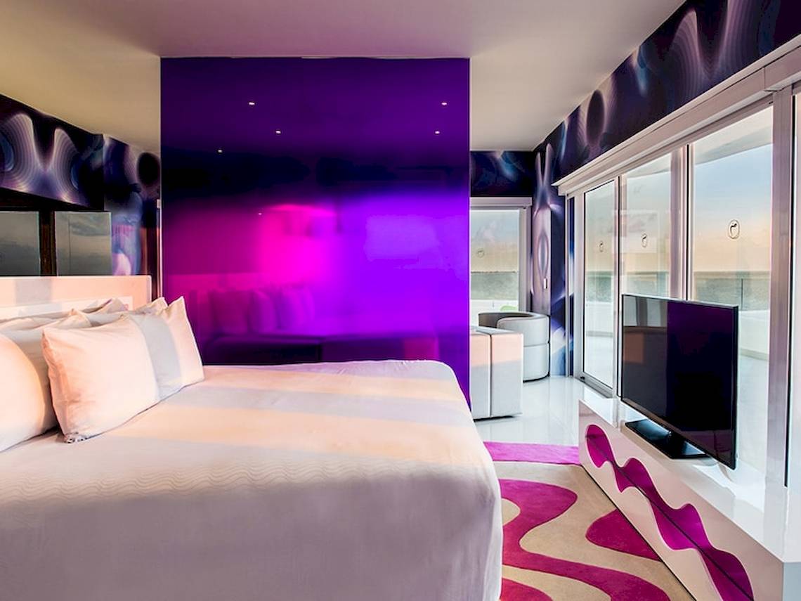 Schlafzimmer im Temptation Cancun Resort mit violetter Wand, Fernseher und Fenstern.