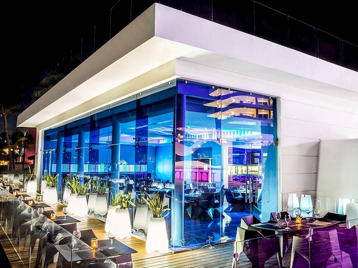 Außenbereich des Temptation Cancun Resorts bei Nacht mit blauen Lichtern und runden Tischen.
