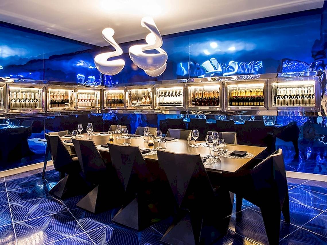 Innenbereich des Temptation Cancun Resort Restaurants mit langem Tisch, blauen Wänden und Flaschen im Kühlschrank.
