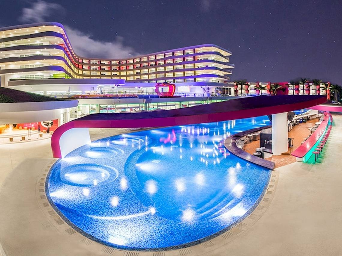 Temptation Cancun Resort Pool bei Nacht mit leuchtenden Farben und Gebäuden im Hintergrund