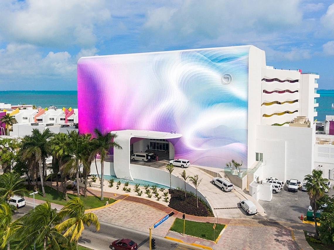 Außenansicht des Temptation Cancun Resorts mit einer großen Wandgestaltung und mehreren Fahrzeugen vor dem Gebäude.