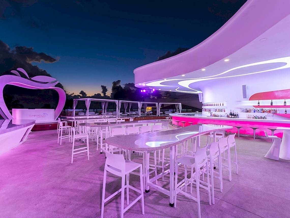 Loungebereich des Temptation Cancun Resorts bei Nacht mit pinker Beleuchtung und Tischen.