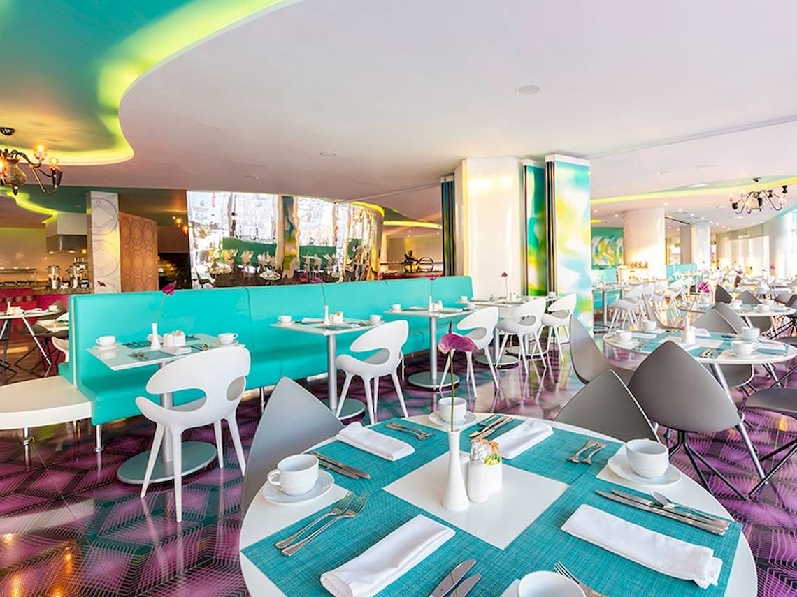 Innenbereich des Restaurants im Temptation Cancun Resort mit blauen und pinken Mustern, weißen Tischen und Stühlen.
