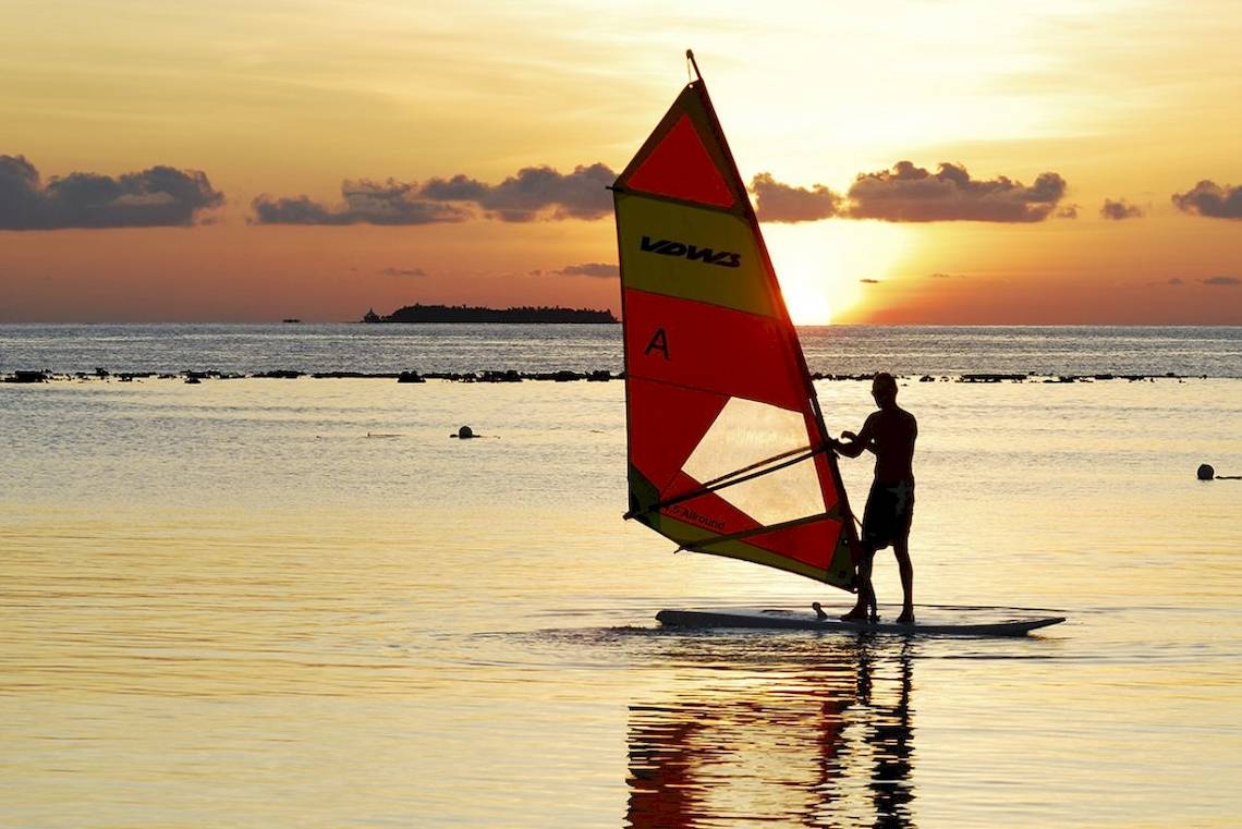 Windsurfer auf einem Segelbrett am Sonnenuntergang im Meer.