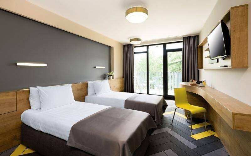 Zwei Doppelbetten mit weißen Kissen und grauen Decken in einem modernen Hotelzimmer.