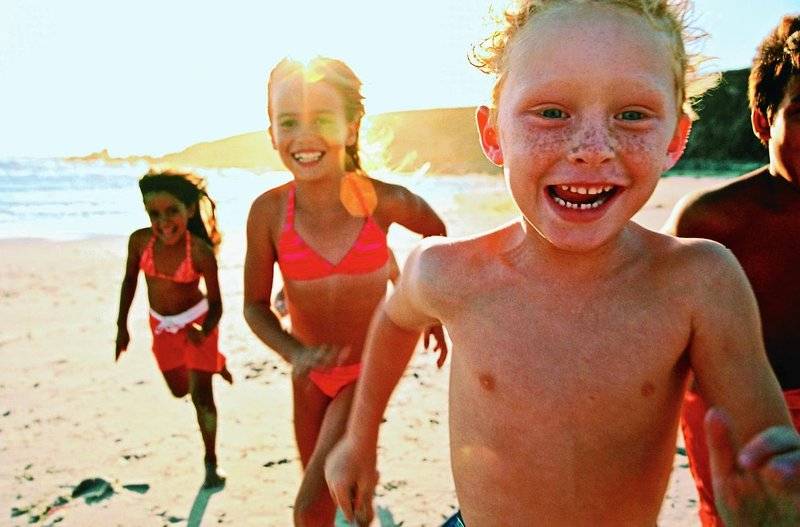 Vier Kinder am Strand, zwei Mädchen und zwei Jungen, alle lächeln und laufen.
