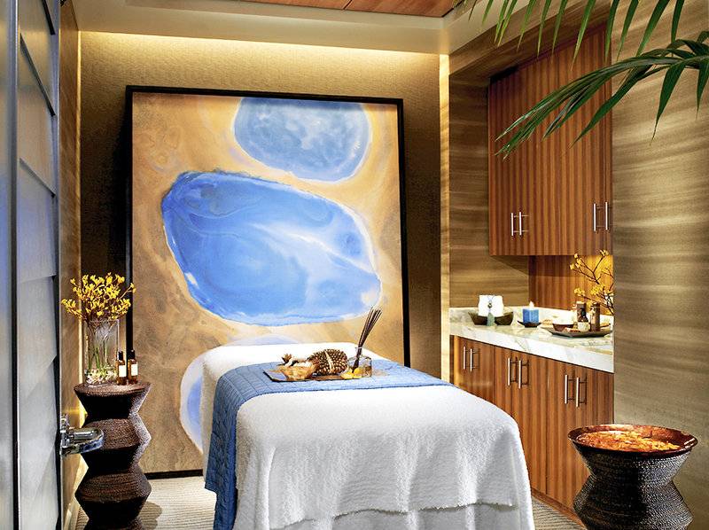 Spa-Behandlungsraum im Caesars Palace mit einem großen Wandgemälde, einem Behandlungstisch, Blumenvase, Kerzen und ätherischen Ölen.