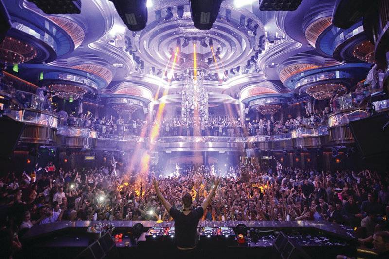Ein DJ spielt in Caesars Palace vor einer großen Menge, die vor einer Bühne steht und Lichtstrahlen und einen Wasservorhang genießt.
