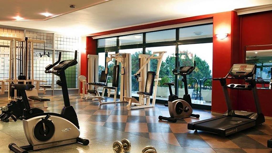 Fitnessraum im Miramare Beach Hotel mit verschiedenen Trainingsgeräten und Blick auf die Außenanlagen.