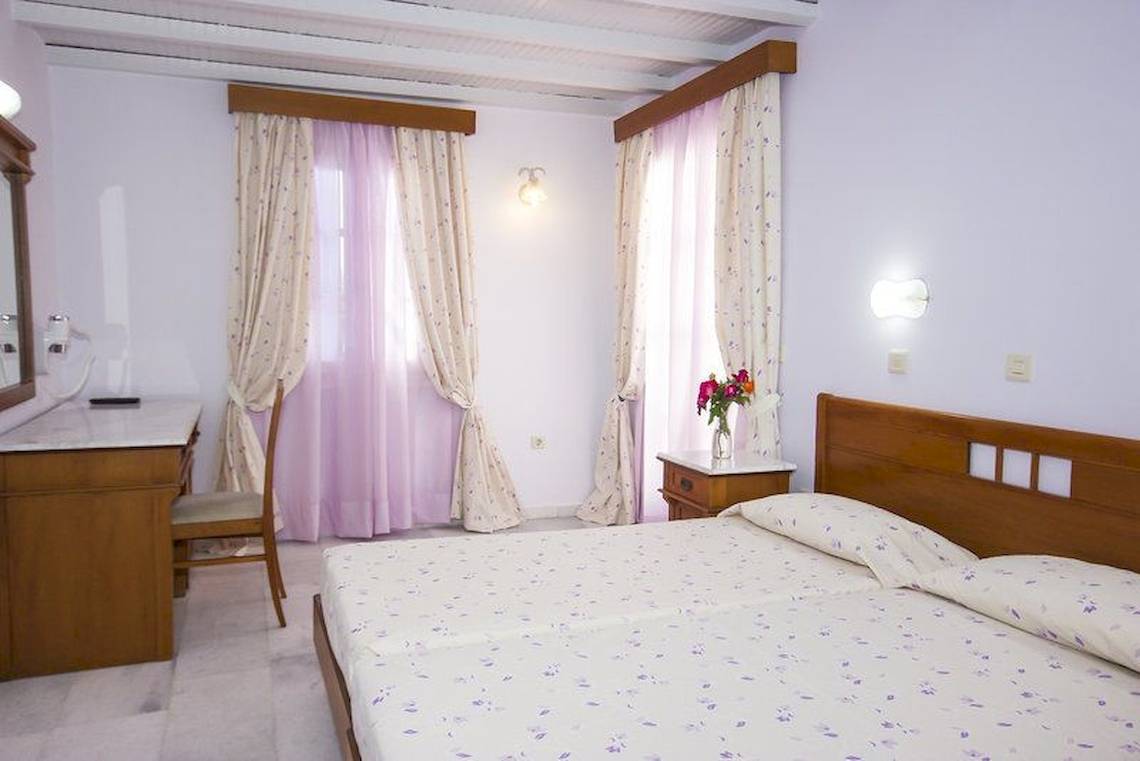 Schlafzimmer mit einem Bett, zwei Kissen, einem Schreibtisch, einem Stuhl, einem Spiegel und einer Vase mit Blumen.