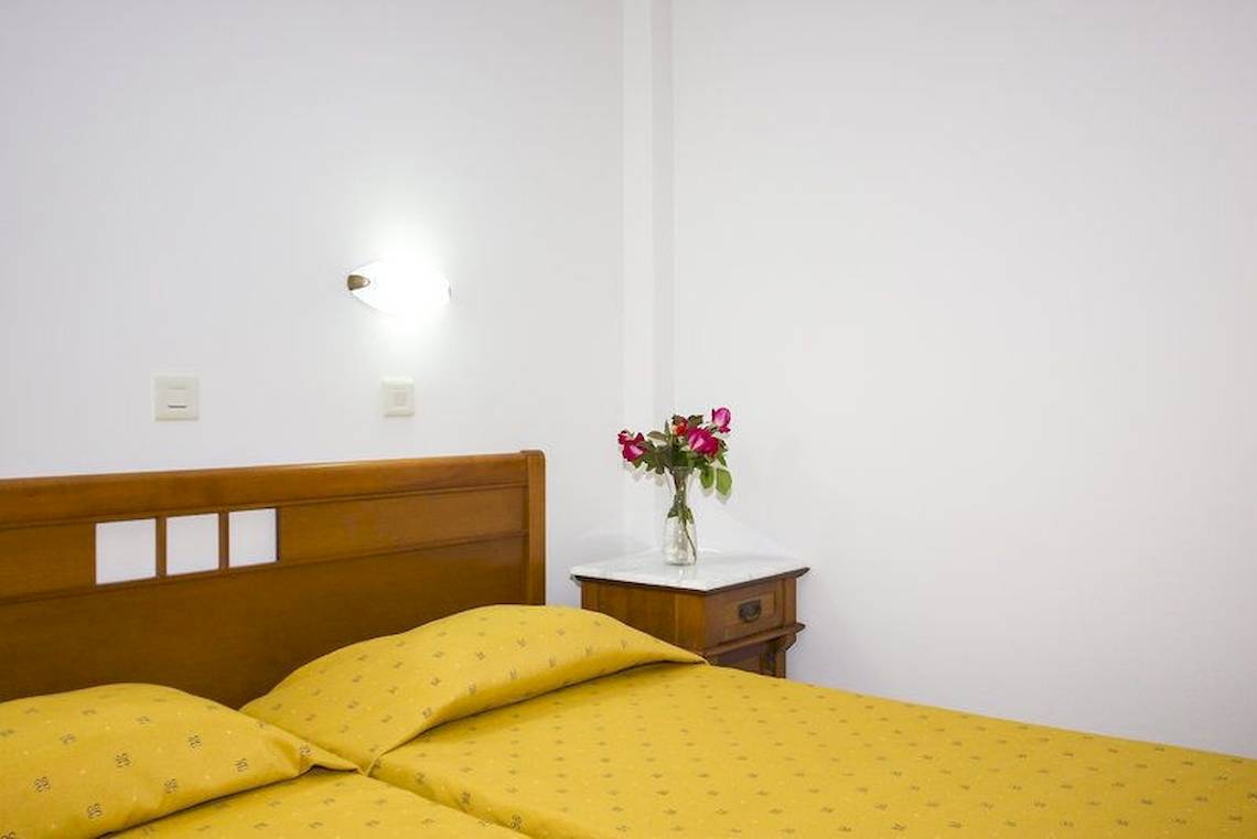 Schlafzimmer mit zwei Betten, Nachttisch und Blumenvase auf weißem Hintergrund.