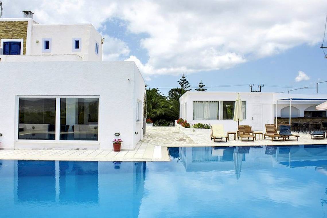 Weißes Hotel Naxos Holidays mit Pool und Lounge-Stühlen im Freien.